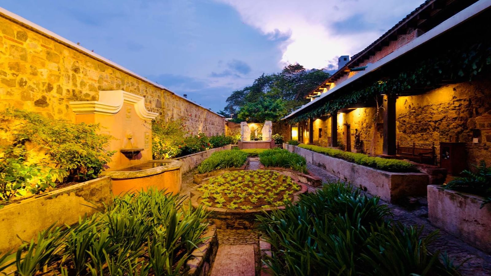 Jardín histórico en Casa Santo Domingo con exuberante vegetación y una fuente iluminada, creando un ambiente tranquilo