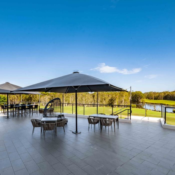 Karinyas Terrace area with tables, chairs, and umbrellas overlooking a serene lake at Mercure Kooindah Waters