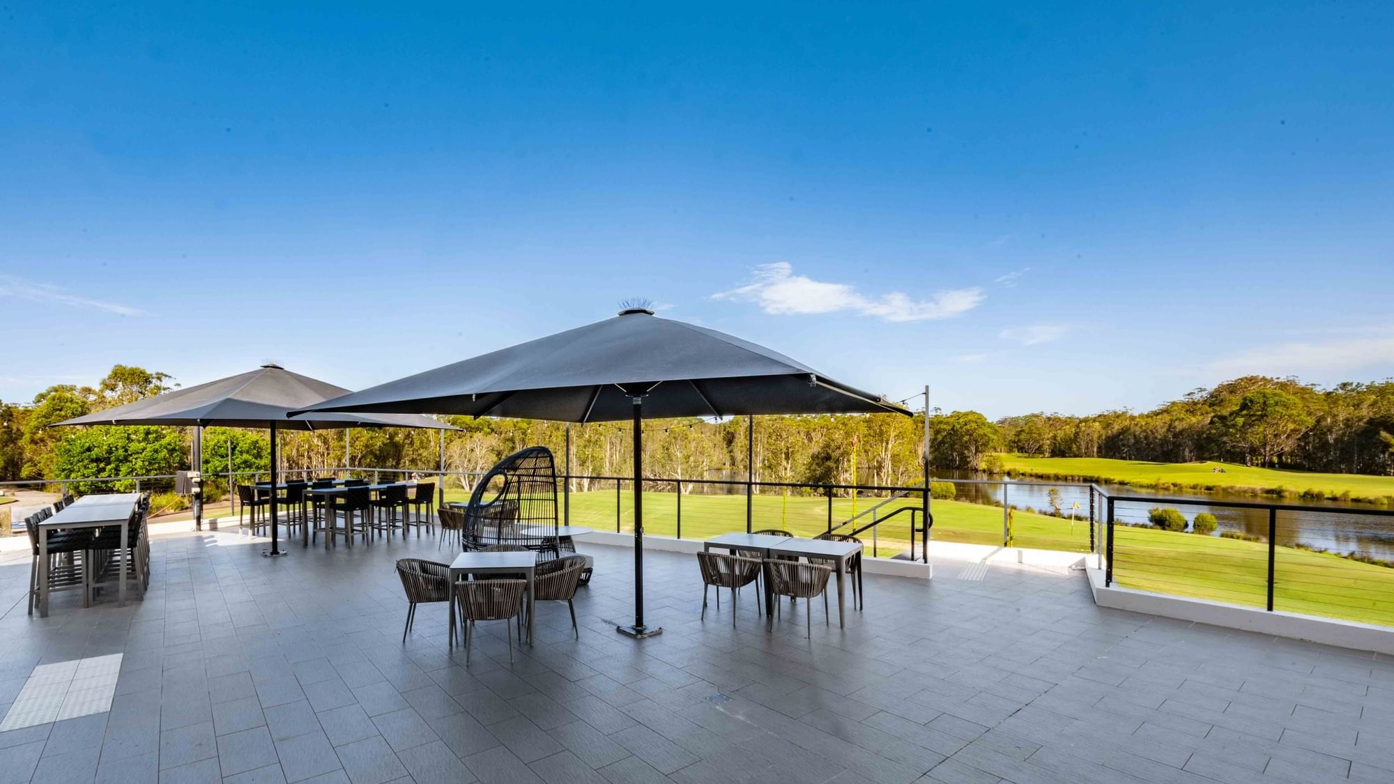 Karinyas Terrace area with tables, chairs, and umbrellas overlooking a serene lake at Mercure Kooindah Waters