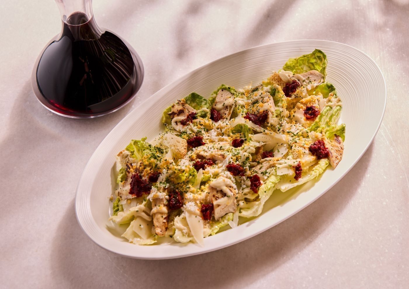 White bowl filled with salad and chicken alongside a decanter of red wine, part of the menu at Whitcombs
