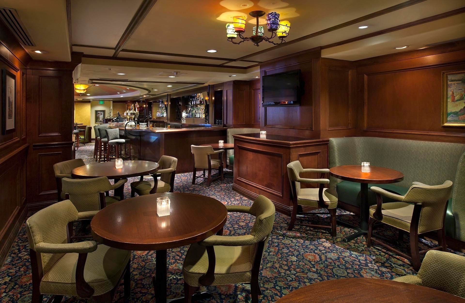 Classic bar & lounge area featuring warm lighting, round wood tables, comfortable armchairs, and a bar at Margaux Restaurant