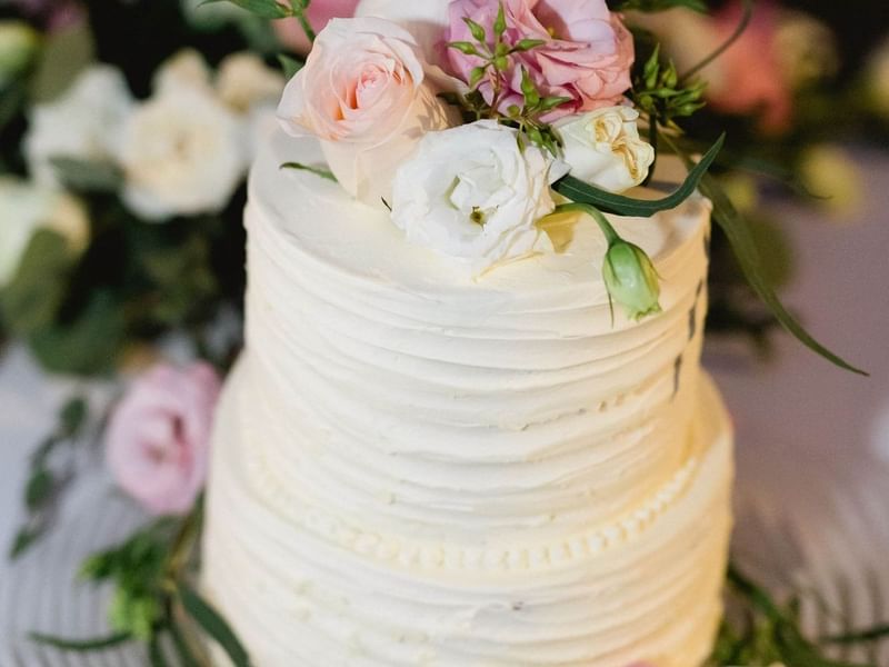 Two-tiered white cake with textured frosting, decorated with pink and white roses and greenery at The Explorean Resorts