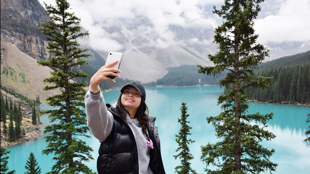 Woman taking a photo in Banff with trees and clouds.