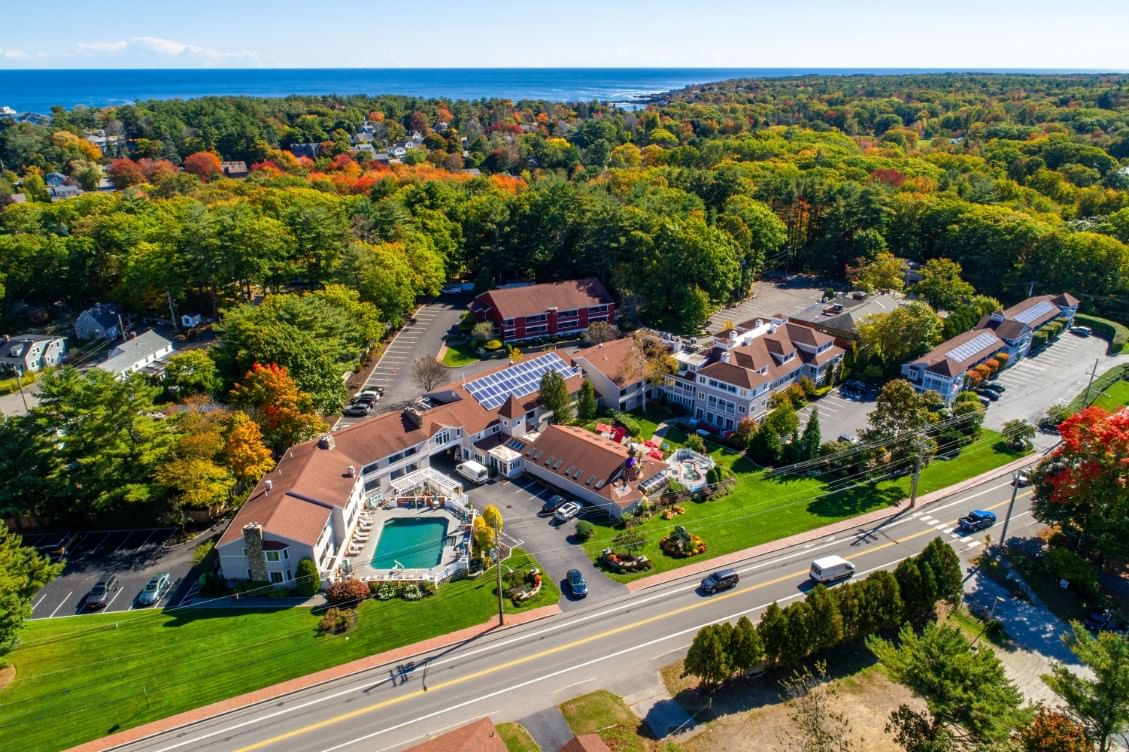 Aerial view of a hotel complex with buildings, parking lot, pool, and trees.