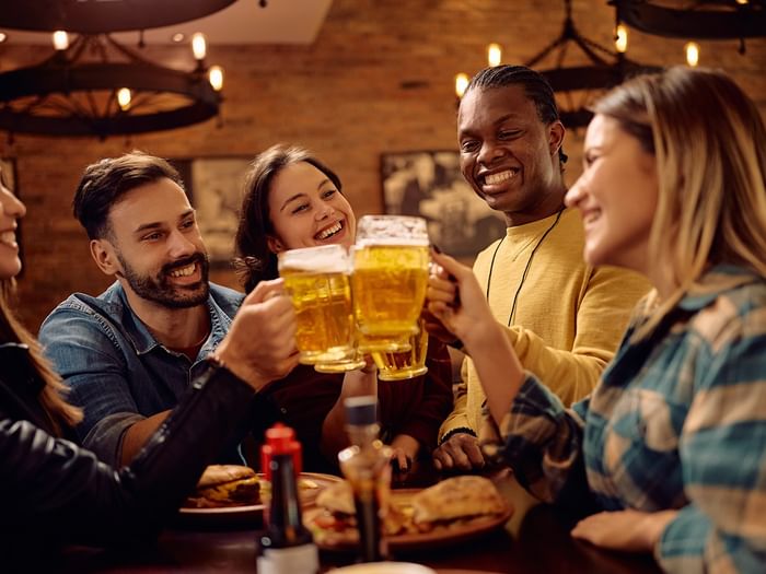 Five friends toast with beers at a restaurant table with food and condiments.