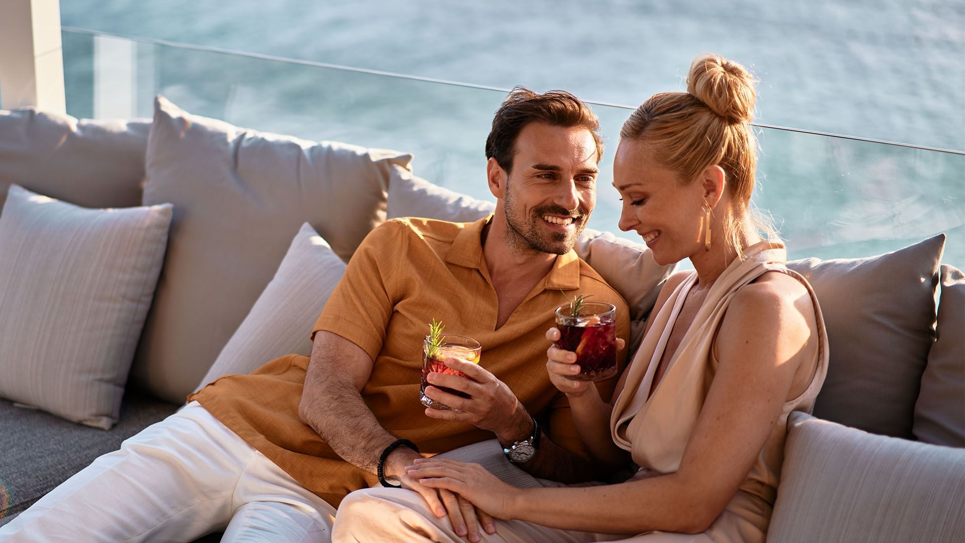 Couple sitting with drinks on a couch by the sea view at Falkensteiner Hotels & Residences