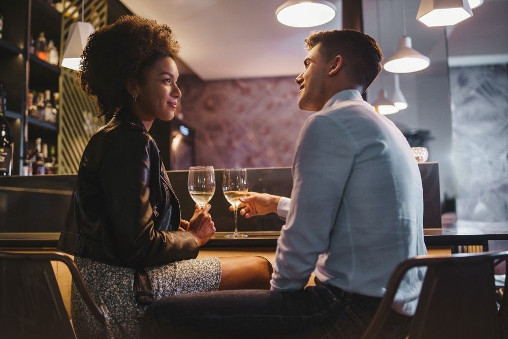 A young man and woman sit facing each other at a bar with wine glasses on a date night on a budget in Orlando.