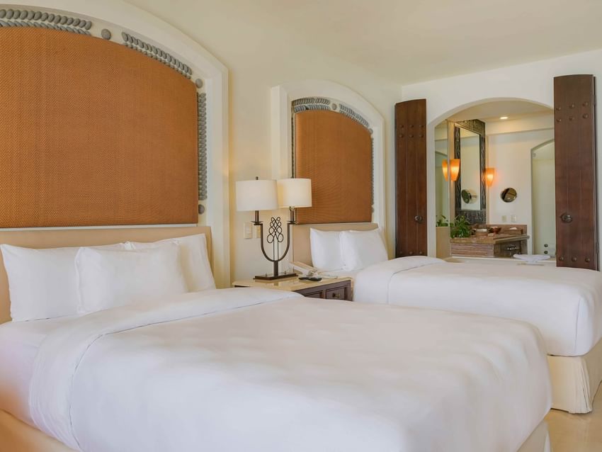 Two comfortable Double beds and a view into the stylish bathroom in Junior Suite Ocean View at Marquis Los Cabos Resort