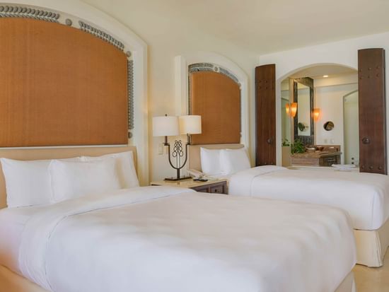 Junior Suite con dos camas dobles, cabeceros texturizados y baño visible en Marquis Los Cabos Resort & Spa.