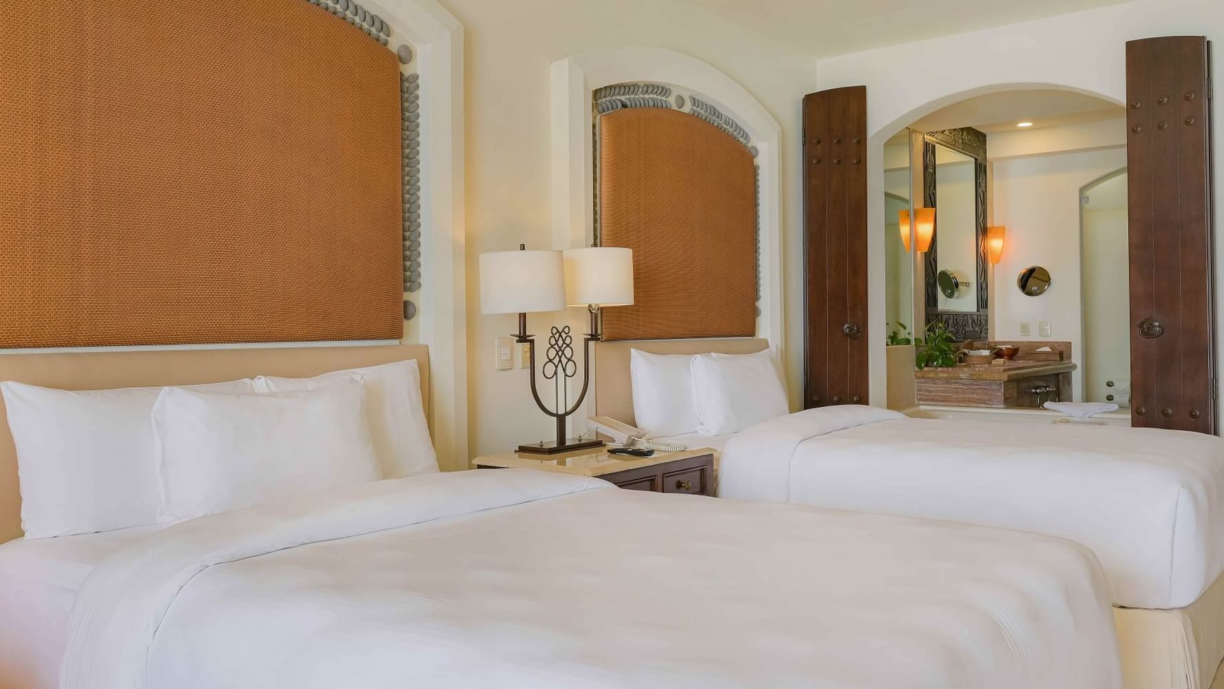 Two comfortable Double beds and a view into the stylish bathroom in Junior Suite Ocean View at Marquis Los Cabos Resort