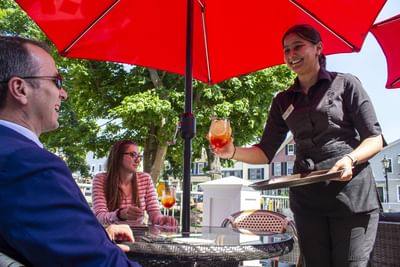 Server offering drinks to guests under a red umbrella at Rodd Charlottetown Hotel, a top choice hotel in PEI