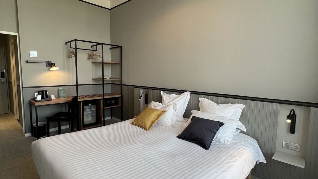 Chambre d'hôtel avec grand lit blanc, bureau et lampes lustre au plafond.