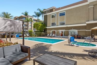 Outdoor pool with lounge chairs by a blue lift under a clear, sunny sky at Anaheim Portofino Inn