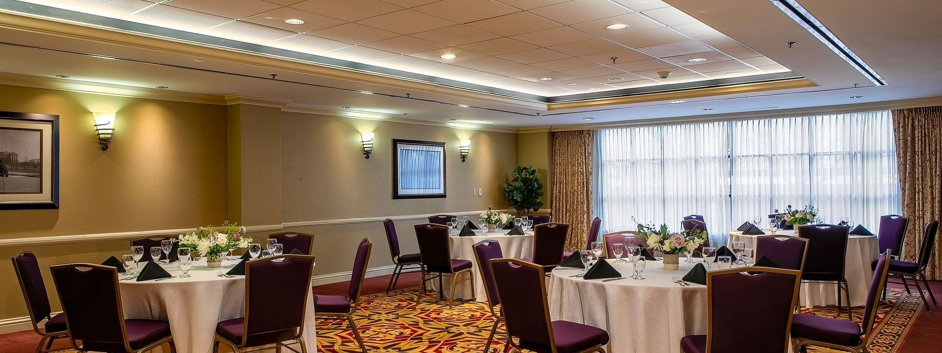 Round tables with white linens and purple chairs in a ballroom by a window in Capitol II/III/IV at Warwick Denver