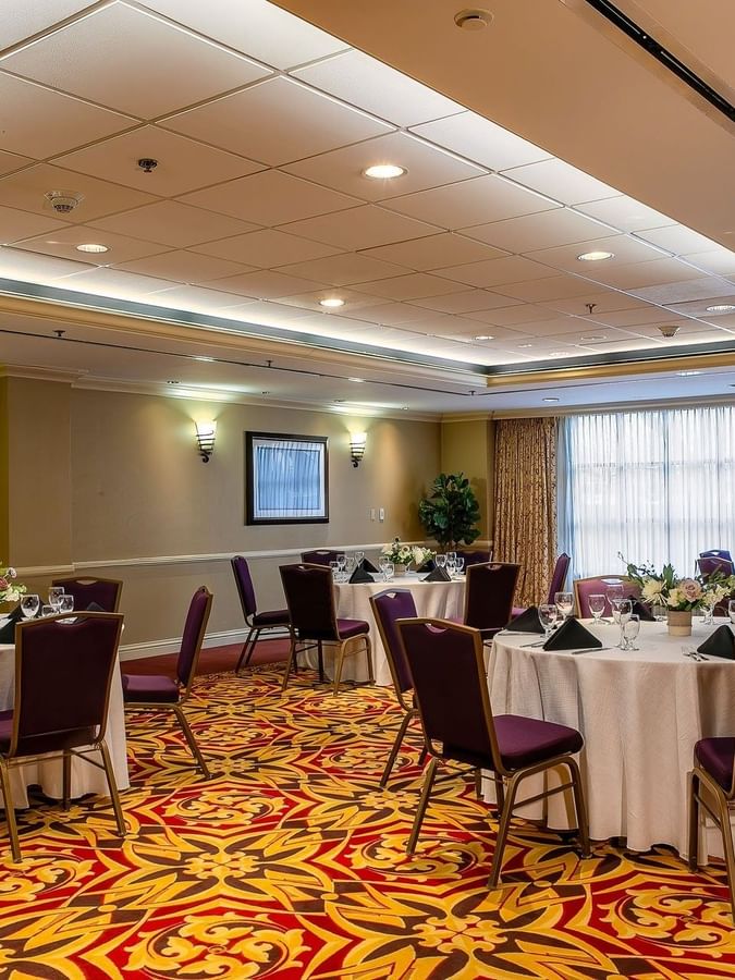 Round tables with white linens and purple chairs in a ballroom by a window in Capitol II/III/IV at Warwick Denver