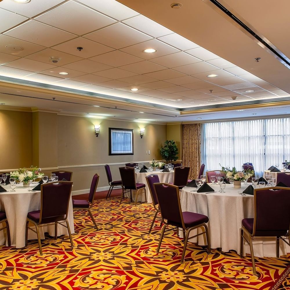 Round tables with white linens and purple chairs in a ballroom by a window in Capitol II/III/IV at Warwick Denver