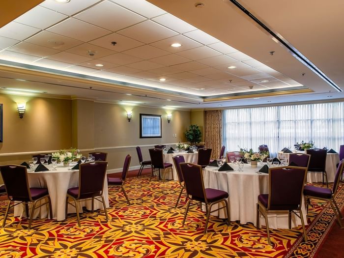 Round tables with white linens and purple chairs in a ballroom by a window in Capitol II/III/IV at Warwick Denver