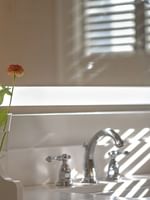 Chrome faucet by a glass vase with flowers under a lighted vanity mirror in Deluxe Suite at Warwick Melrose Dallas