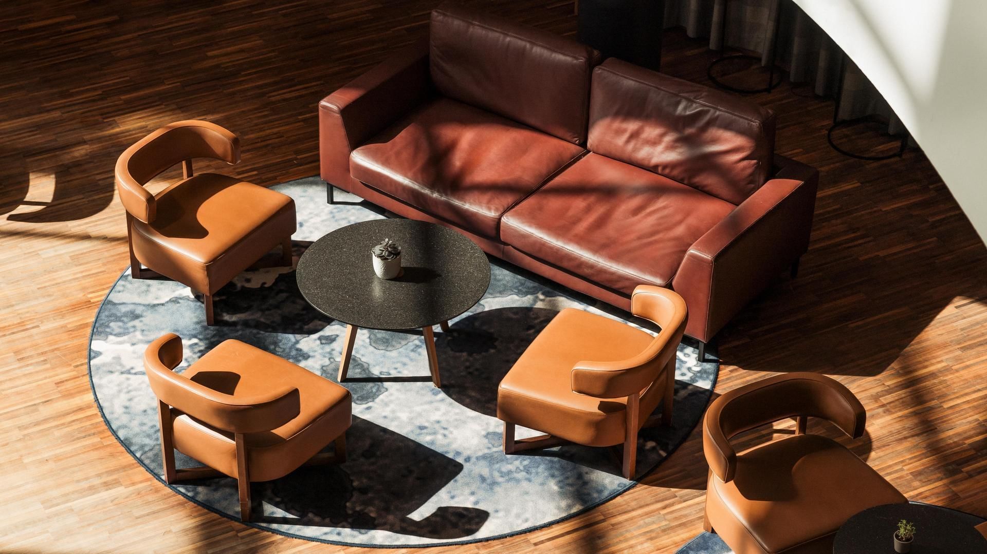 Braune Couch und vier Sessel um einen runden Tisch auf einem blauen Teppich angeordnet.