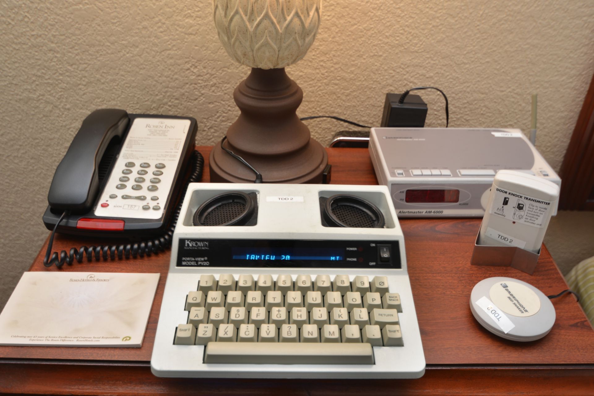 a desk with a telephone, typewriter, alarm clock, radio and hotel paper