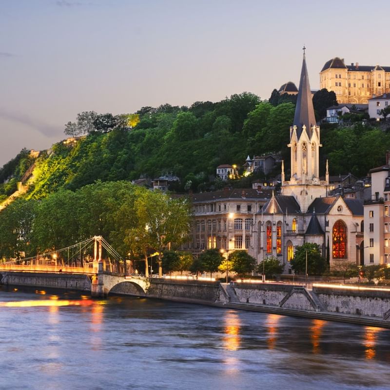 Scenic view of a riverside Lyon city, featuring a tall church spire, and vibrant buildings near Warwick Hotels and Resorts
