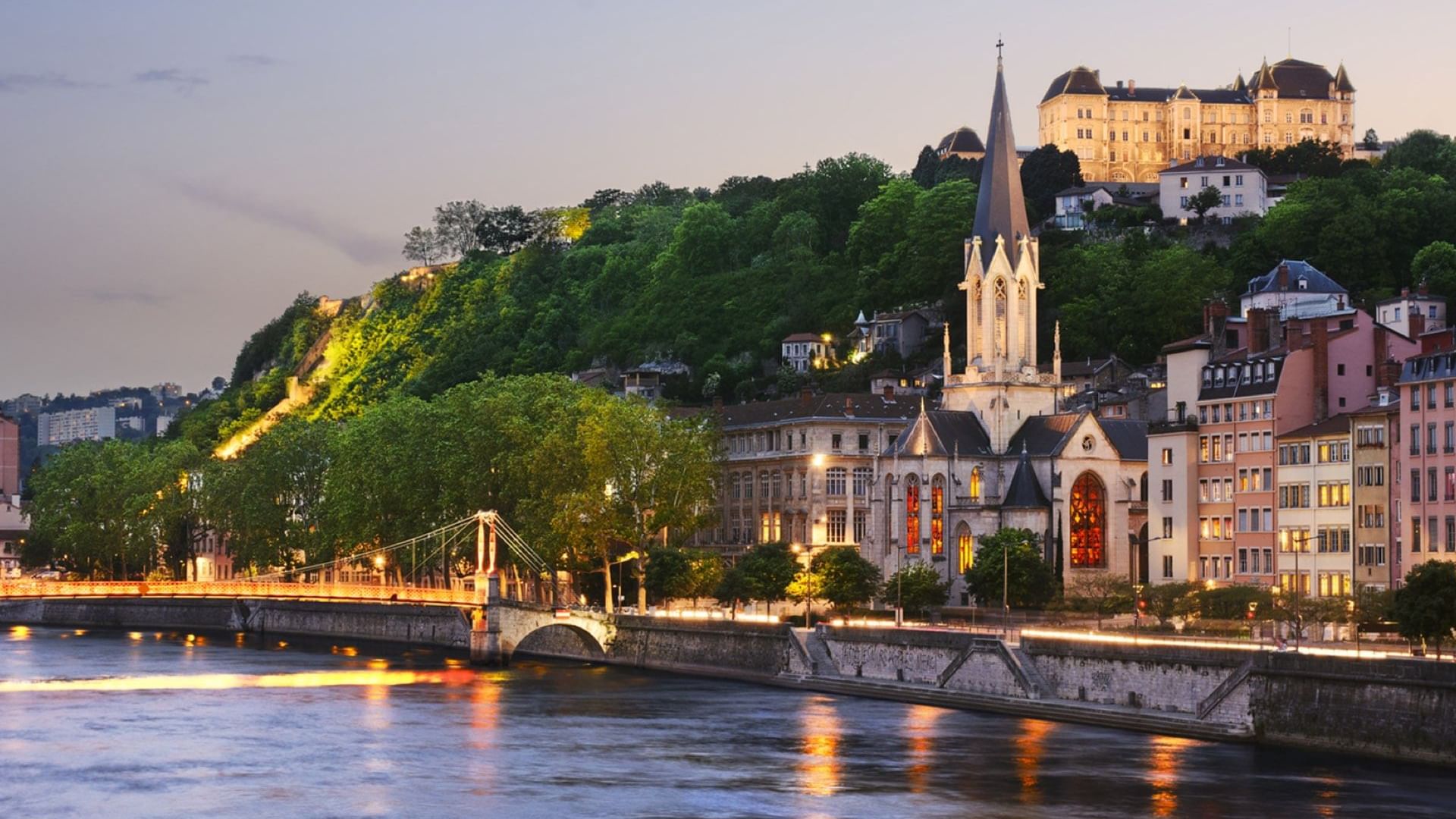 Scenic view of a riverside Lyon city, featuring a tall church spire, and vibrant buildings near Warwick Hotels and Resorts