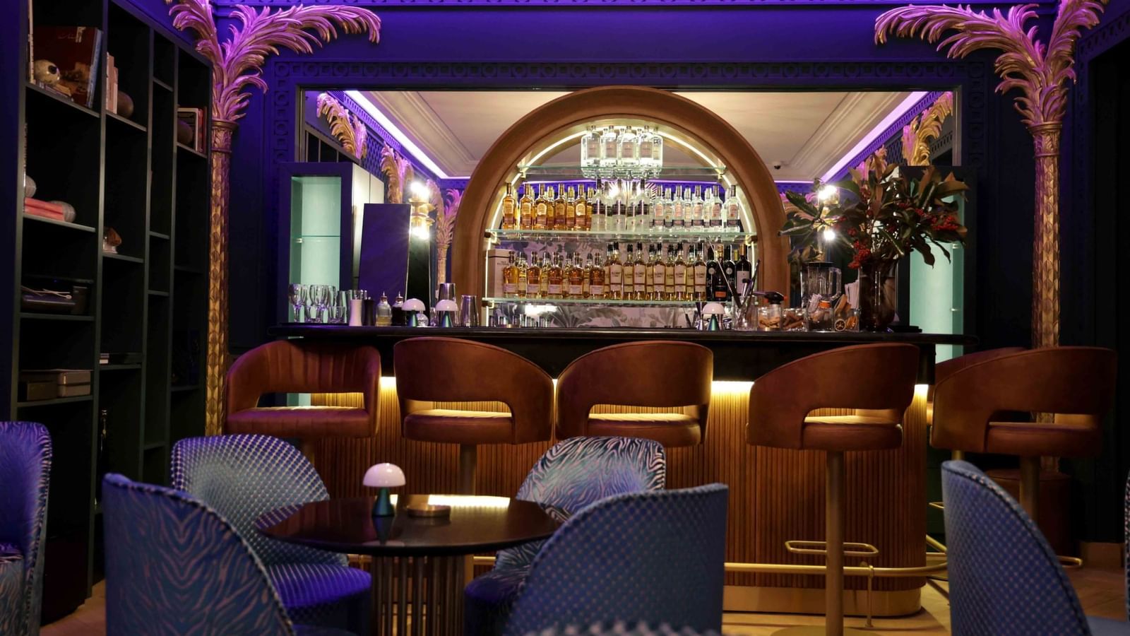 Blue seating by the bar counter with liquor shelves at The Bar in Warwick Palm Beach Hotel