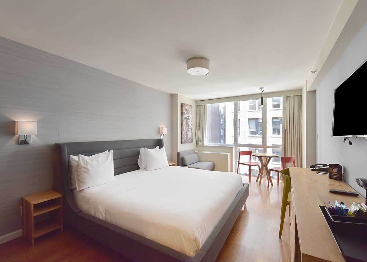 A wide view of a hotel room with a bed, desk, chair, and TV