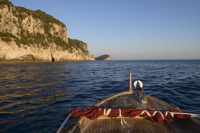 Wooden boat bow sailing past dramatic coastal cliffs under clear blue sky at Grand Hotel Portovenere
