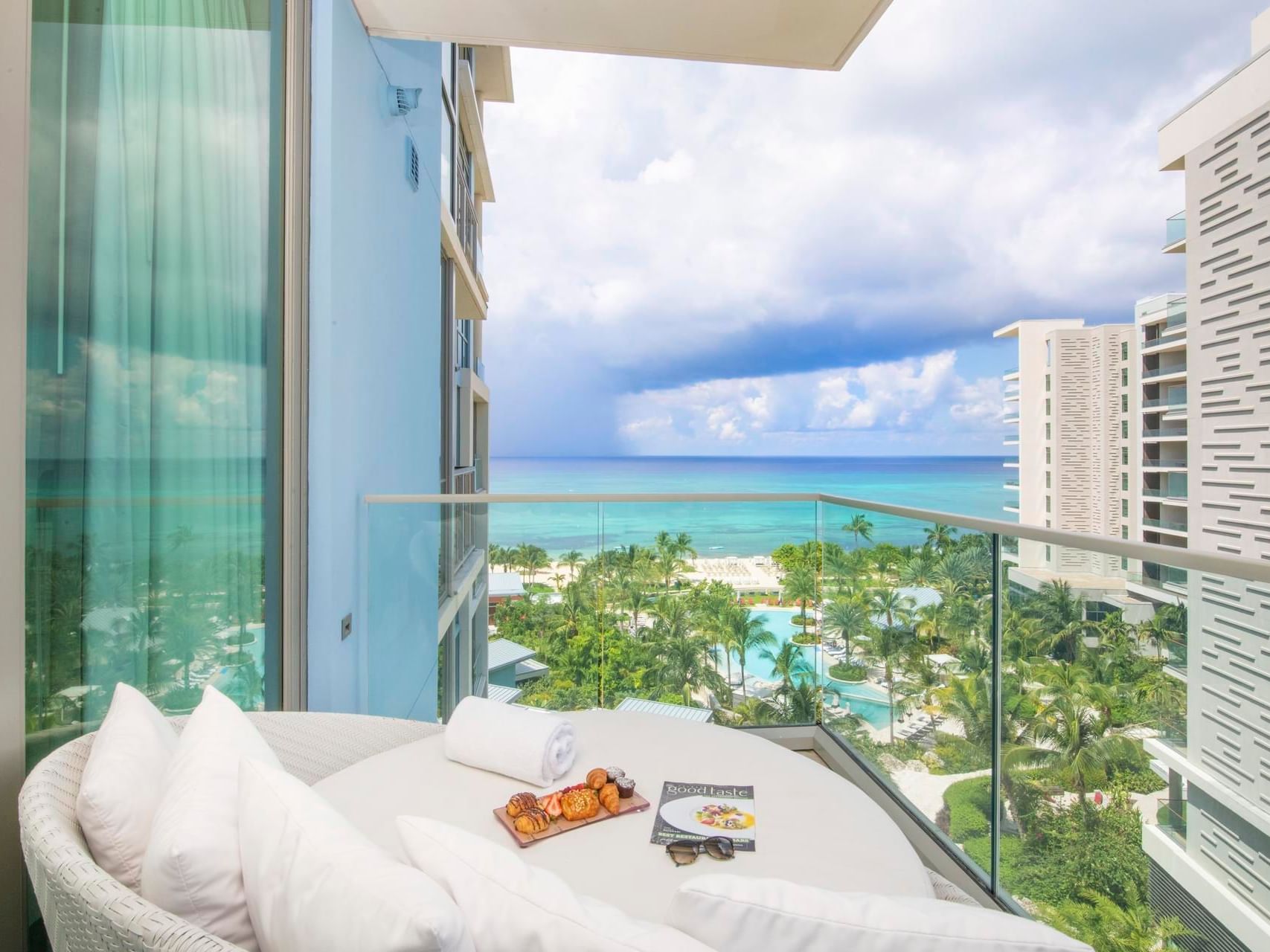 Balcony view with a plate of pastries and a magazine, overlooking palm trees and the sea in N703, The Residences at Seafire.
