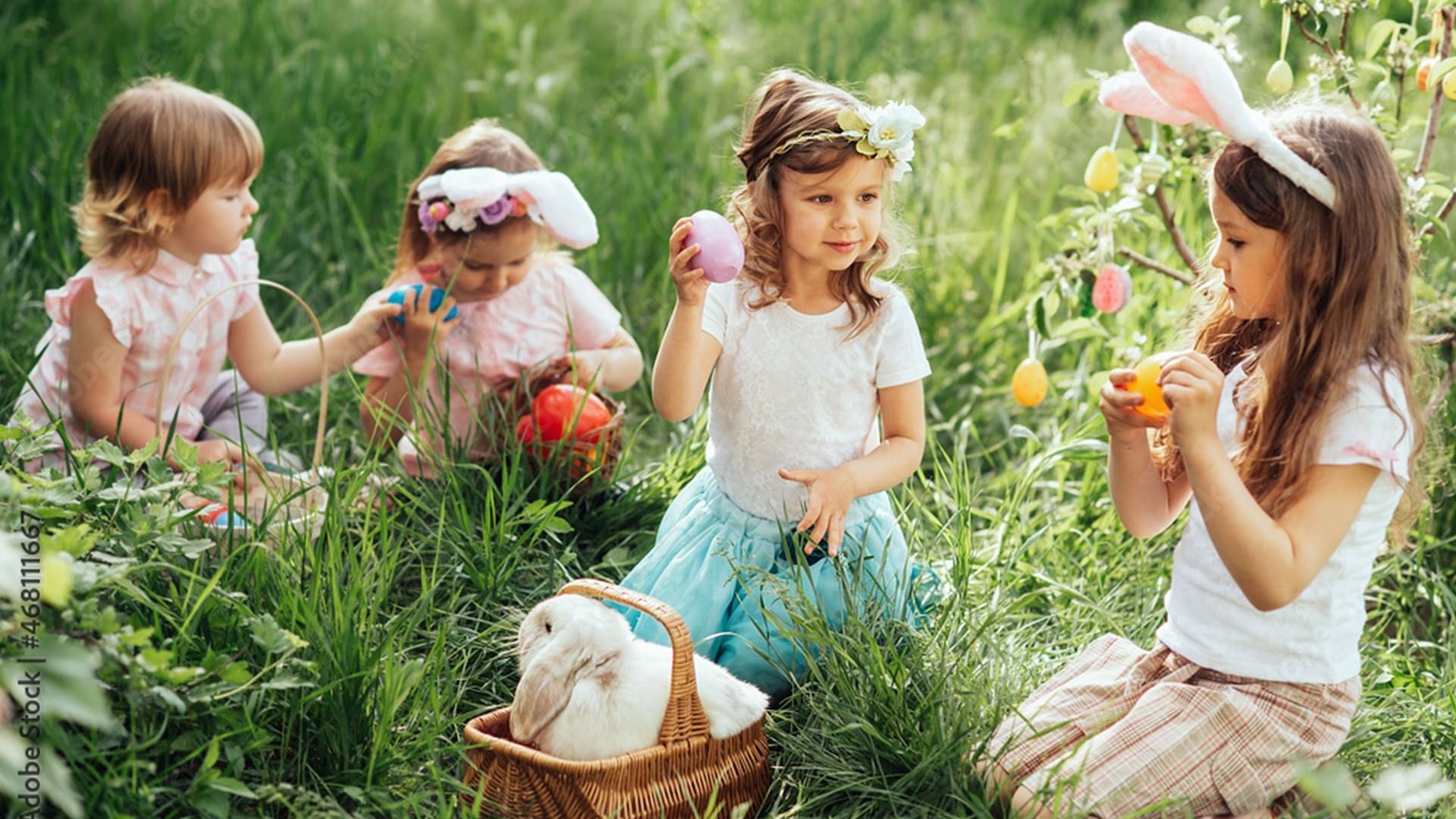 Quattro bambine con uova di Pasqua e coniglio in cestino nell'erba di Falkensteiner Group