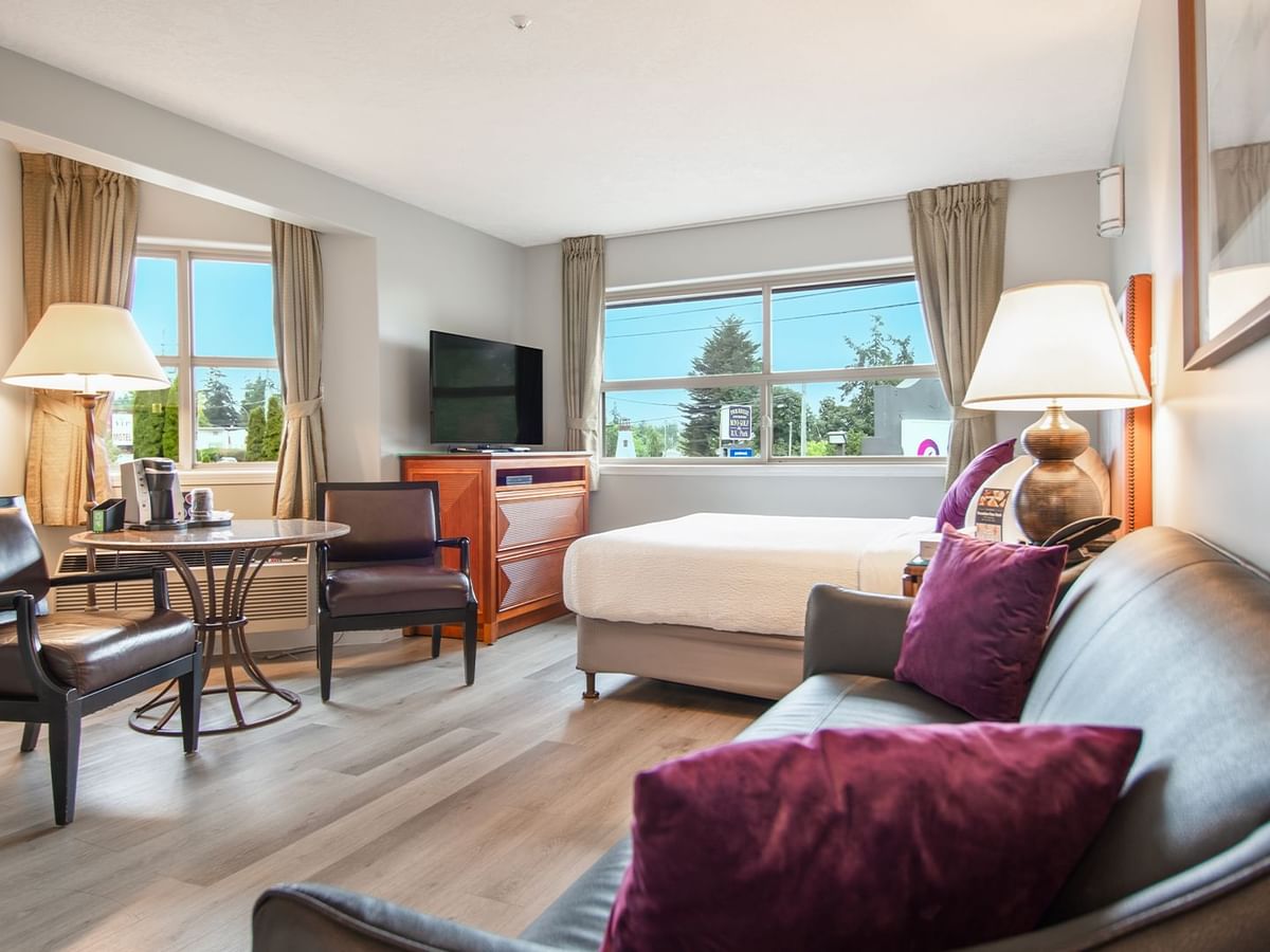 A hotel studio suite with queen bed, couch, TV, table and chairs