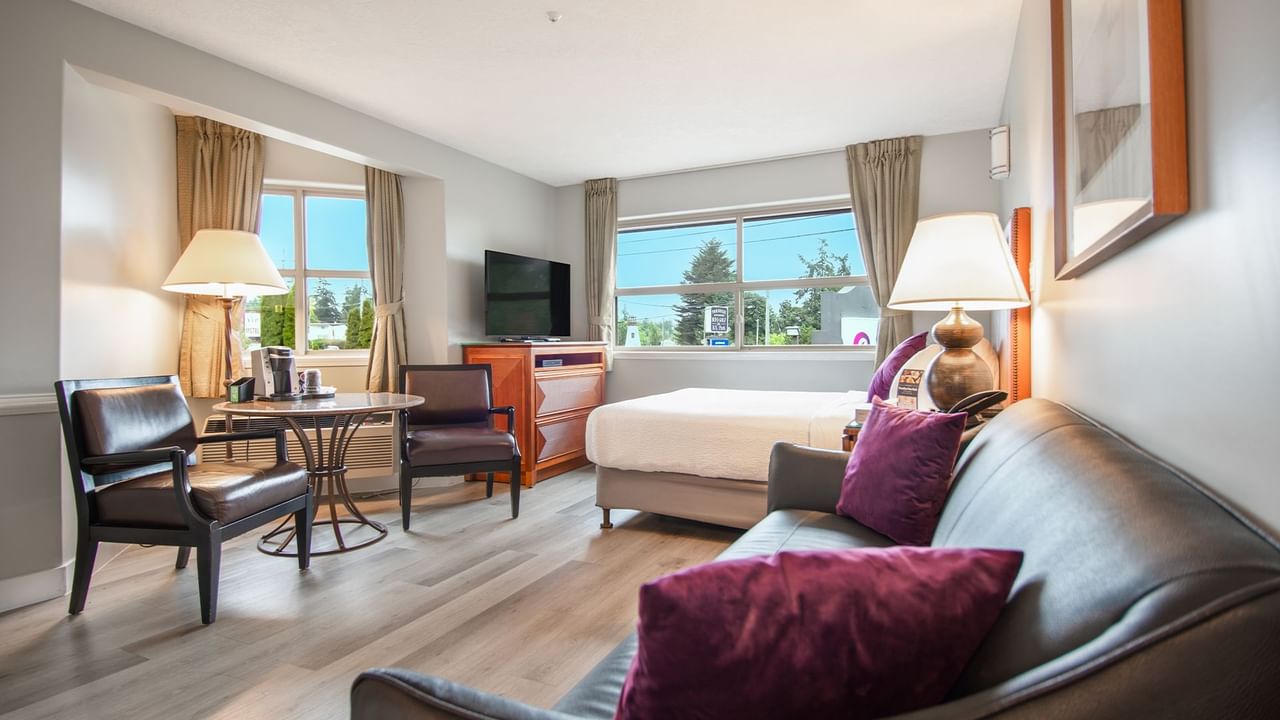 A hotel studio suite with queen bed, couch, TV, table and chairs