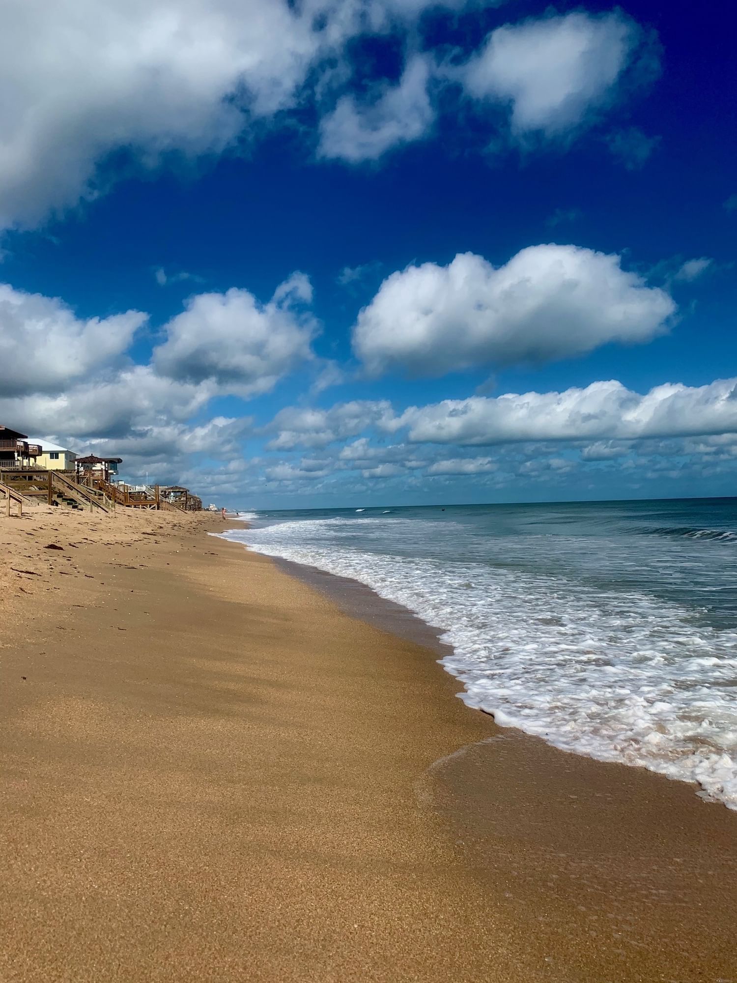 A shoreline with sand, ocean, and a deep blue sky with clouds.