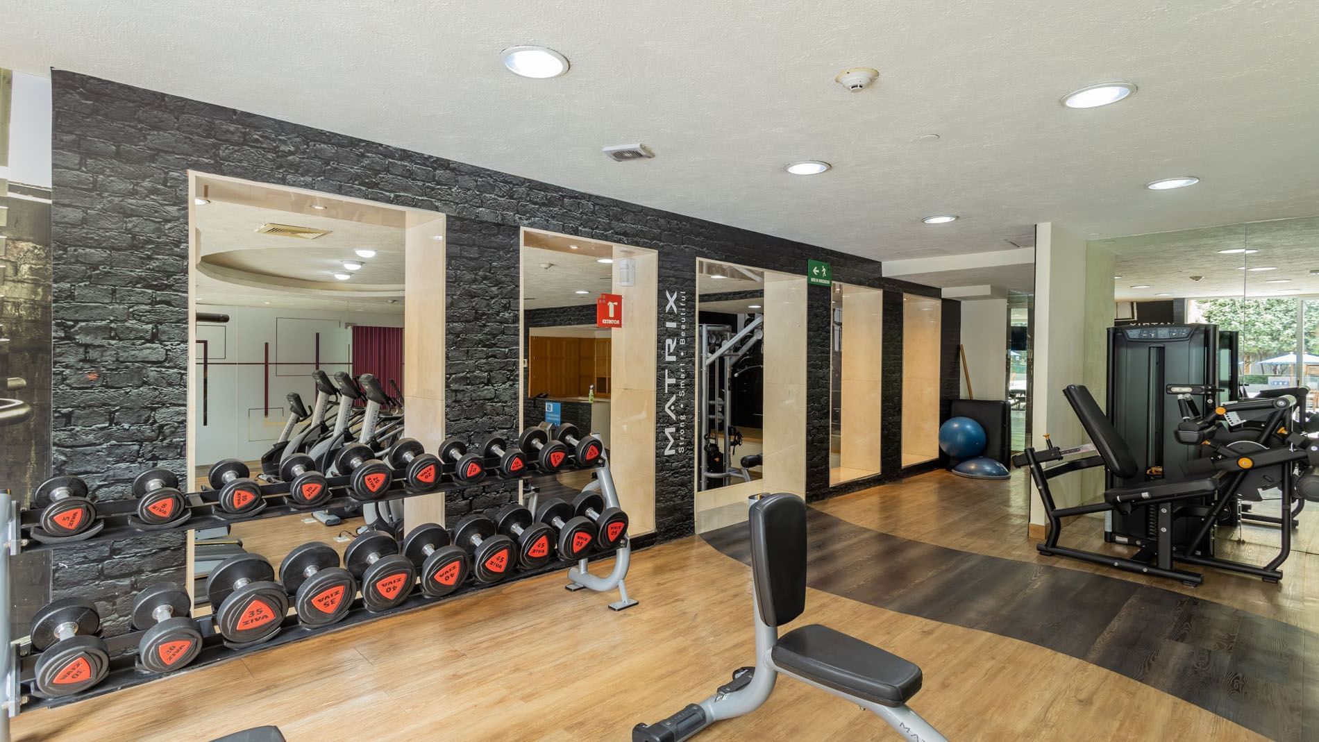 Modern fitness center with organized dumbbells and a black brick accent wall at Camino Real Polanco Mexico