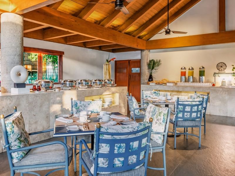 Chic dining area with cozy chairs, set table, buffet with chafing dishes, and natural light at Grand Fiesta Americana