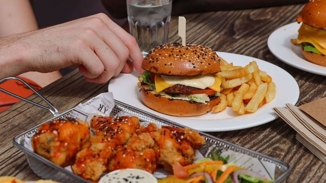 Hand reaching for a hamburger with fries and spicy wings in The Brewery Bar + Kitchen at Novotel Sydney Olympic Park