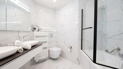 Modern bathroom with two sinks, a toilet, and a glass-enclosed bathtub.