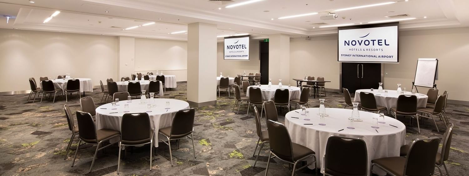 Protea Conference Room set with banquet tables facing a projector screen at Novotel Sydney International Airport