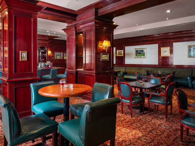 A restaurant with wooden tables, blue leather chairs, and red columns, featuring a bar and framed artwork.