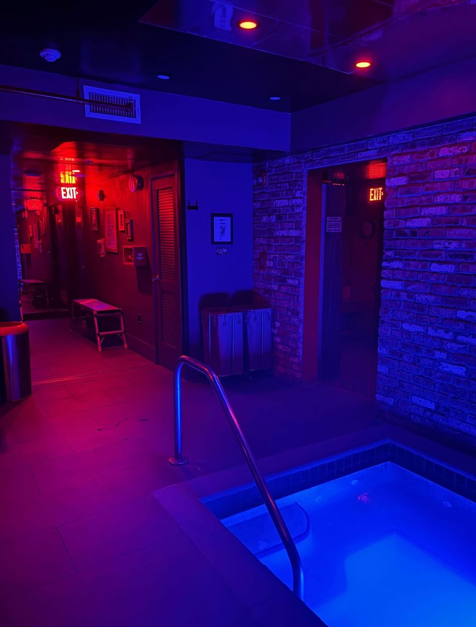 Another angle of the dimly lit spa area with purple and red lights, featuring a jacuzzi and brick walls at The Gaythering