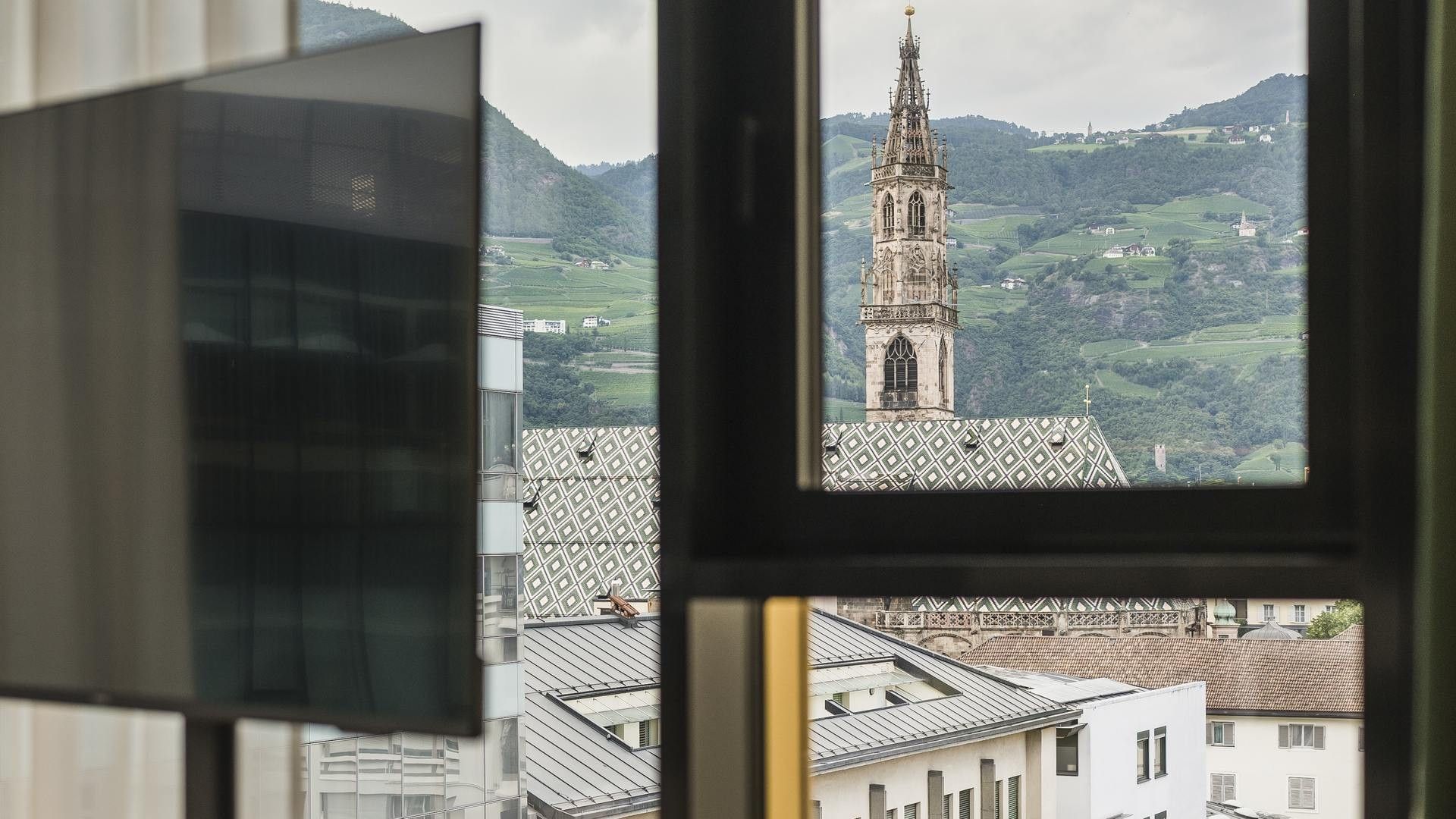 A window view from indoors shows a tower, buildings, and distant mountains.