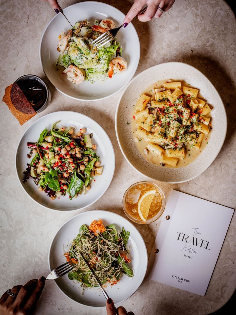 Four plates of assorted dishes with a by day menu from The May Fair Bar