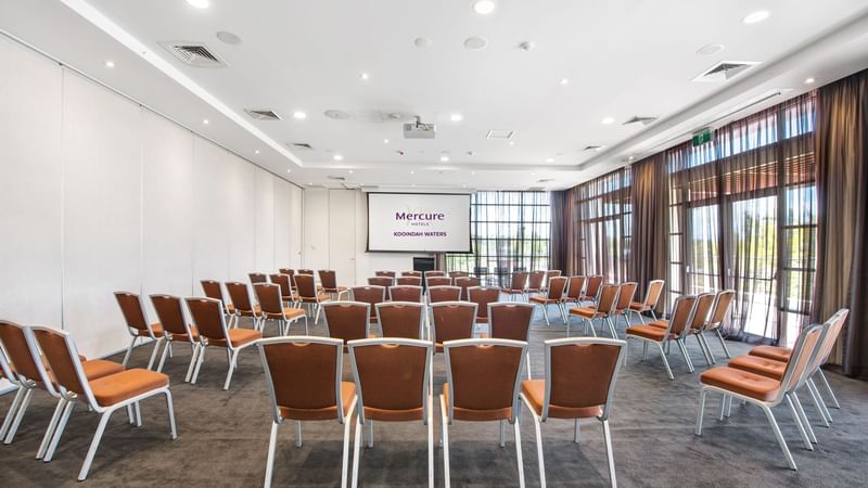 Kooindah One Meeting room with rows of orange chairs facing a projector screen at Mercure Kooindah Waters