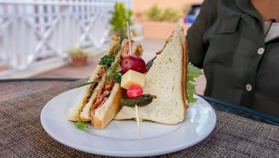 Large double-decker club sandwich with a side garnish on a white plate and wood table at Worthing Court Apartment