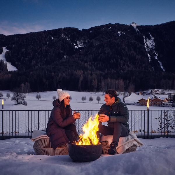 A Couple warming with a bonfire & coffee, Falkensteiner Hotels