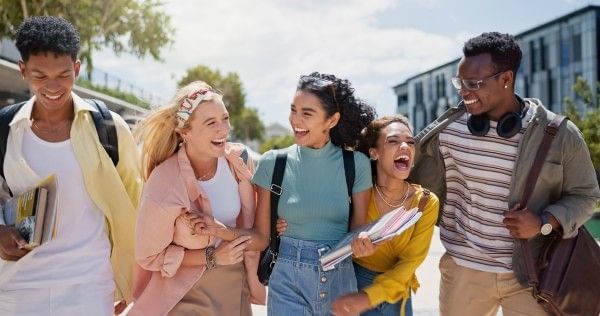A group of five smiling, happy college students walking outdoors with textbooks in hand.