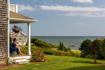 Woman relaxing on a chair on a beachfront porch with garden & enjoying the view of a boat in the sea at Chatham Tides Resort