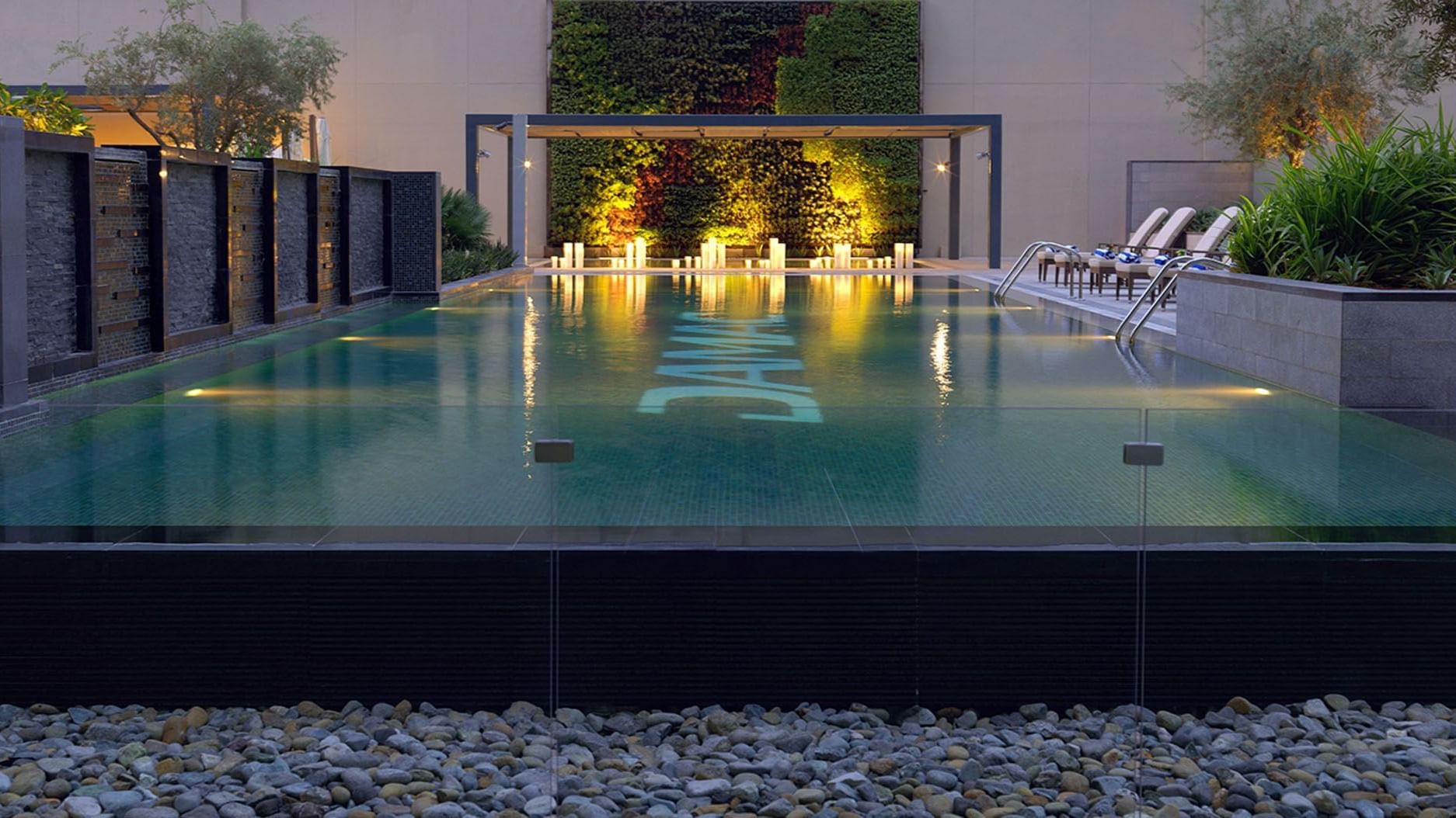 Outdoor pool area with illuminated lights & lounge chairs at DAMAC Maison Cour Jardin