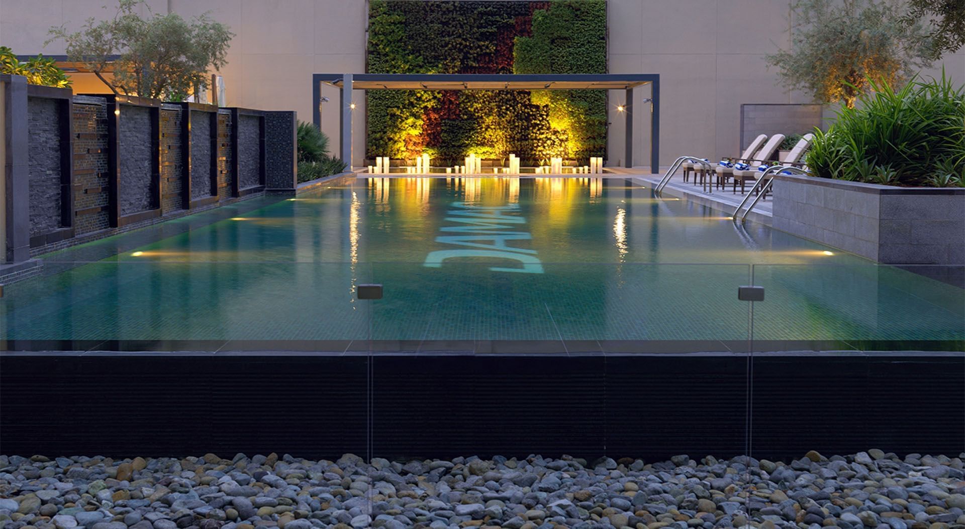 Modern outdoor pool at dusk with lighting and lounge chairs in DAMAC Maison Cour Jardin